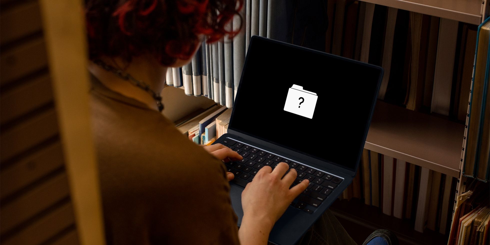 Une femme assise à son bureau, dépannant un ordinateur portable MacBook Air qui affiche un point d'interrogation à l'écran pour avertir d'une erreur de disque de démarrage